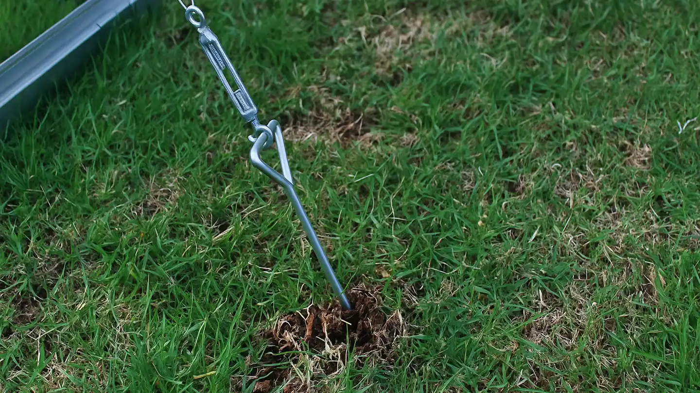 Greenhouse anchor kit fastened into a grass field